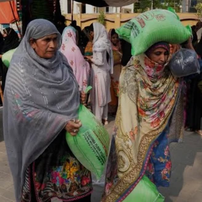 Two women carrying green flour bags home from the distribution